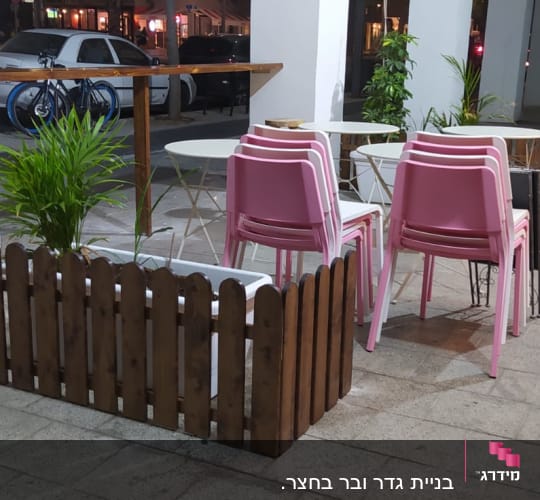 גדר עץ קטנה ליד שולחנות וכיסאות ורודים